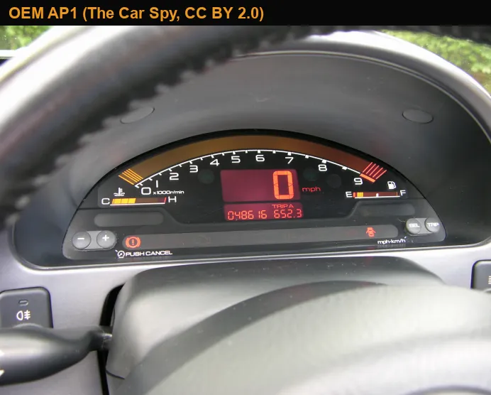 Lit Honda S2000 AP1 cluster photographed through the steering wheel, with the amber tach band, red speed readout and horizontal temperature and fuel bars